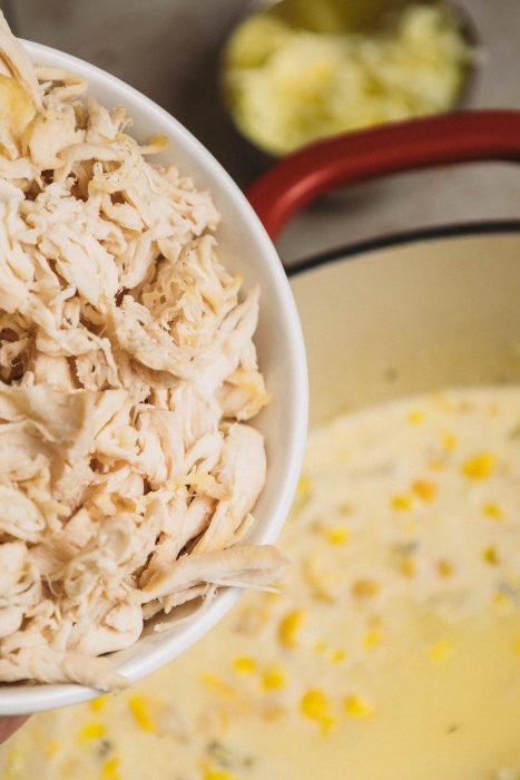 Shredded chicken in a bowl next to a pot of soup.