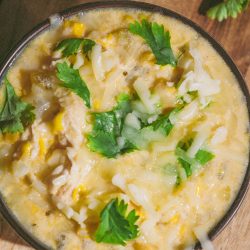 A bowl of soup with cheese and parsley on a wooden table.