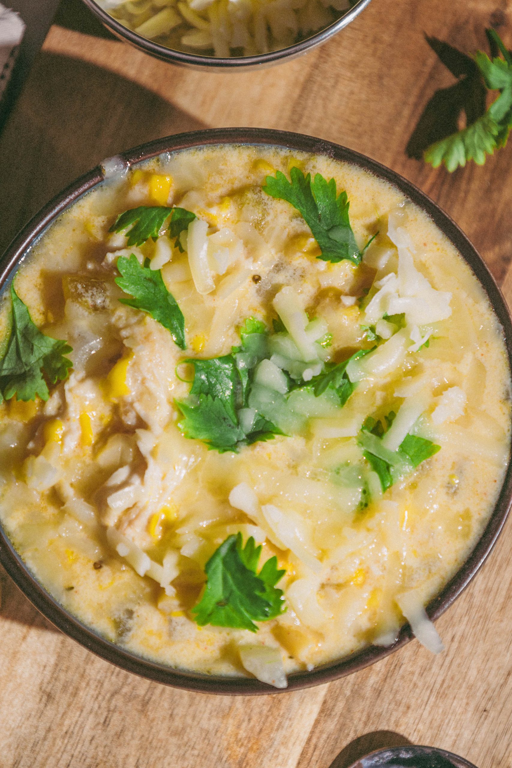 A bowl of soup with cheese and parsley on a wooden table.