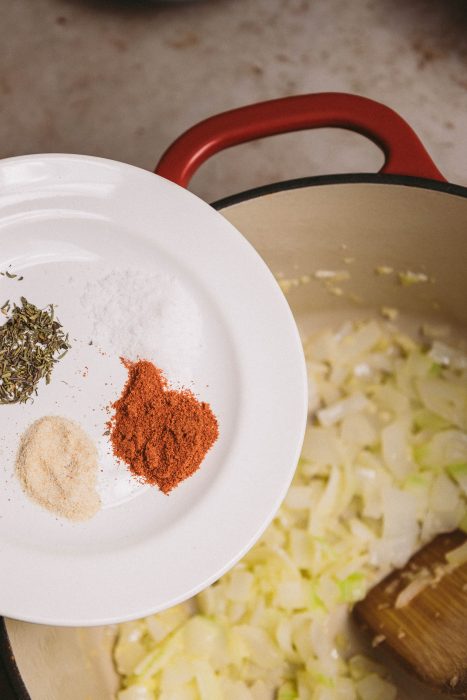 A white plate with spices on it next to a wooden spoon.