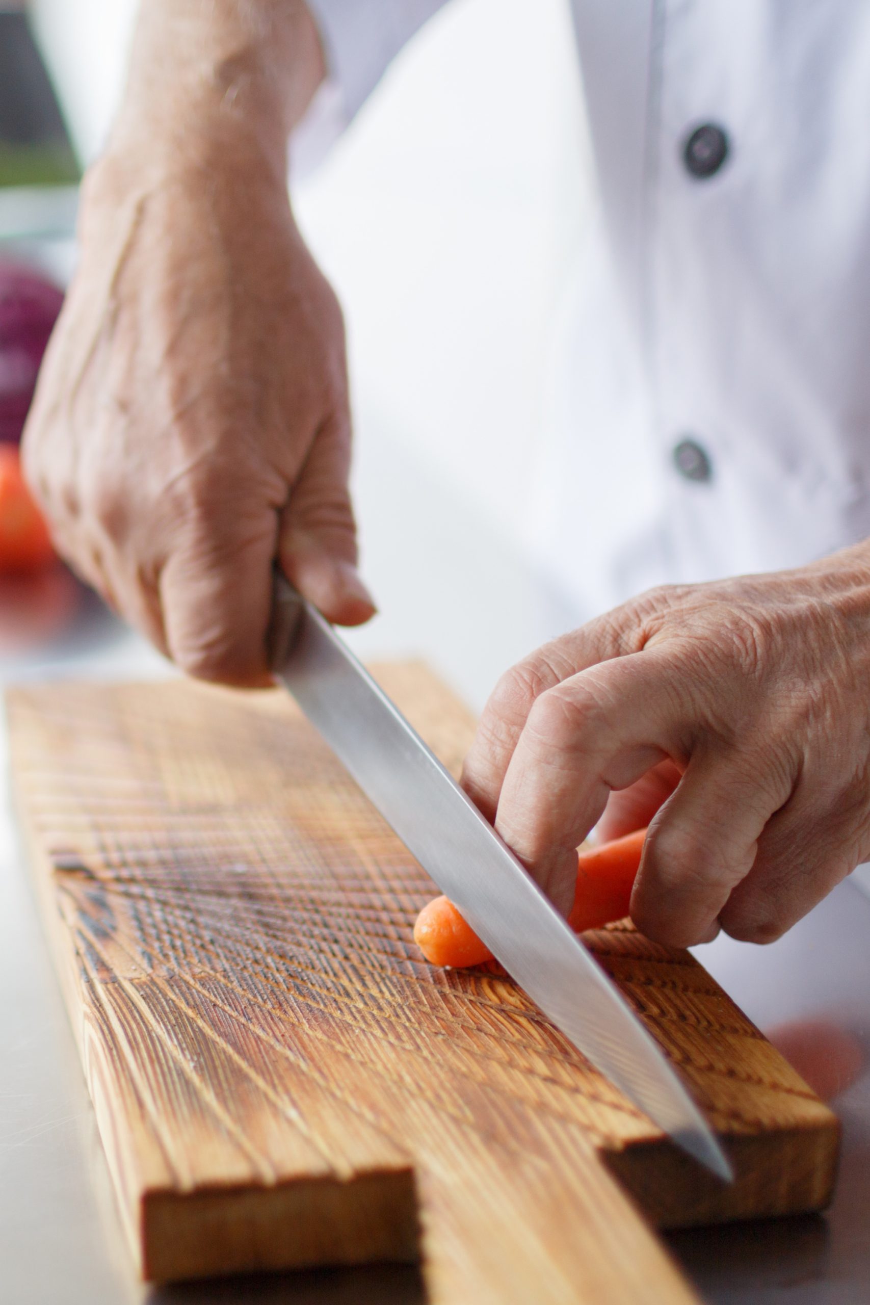 Best kitchen knives. A chef cutting a carrot on a wooden cutting board.