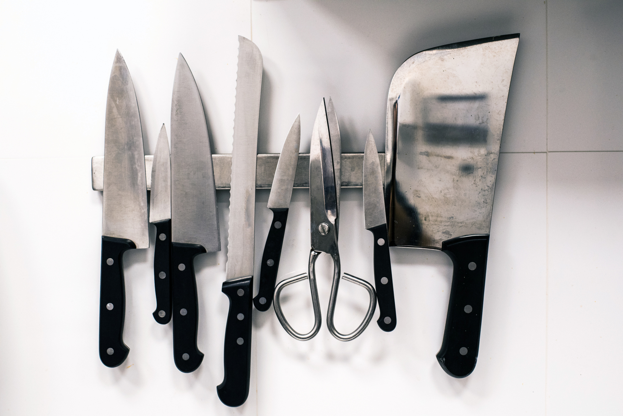 A group of knives and a pair of scissors hanging on a wall.