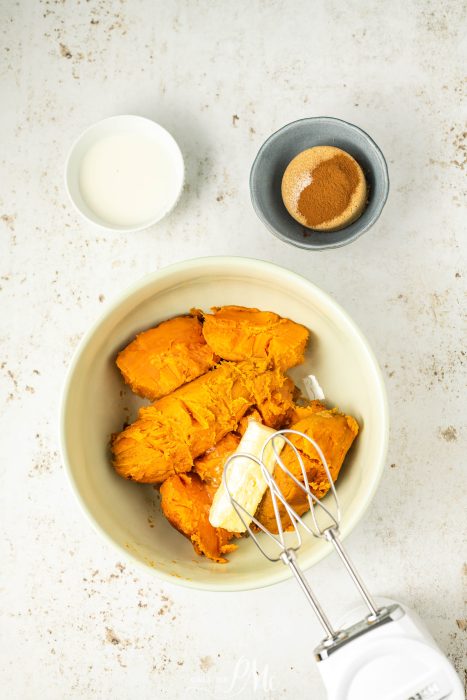 Mashed sweet potatoes in a bowl with a mixer and butter.