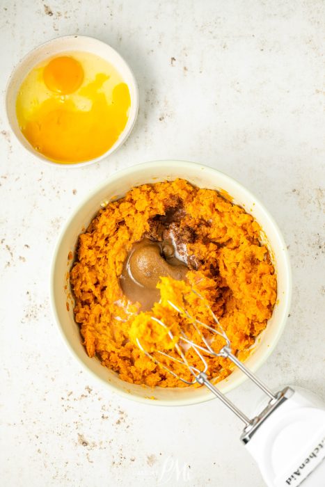 A bowl of sweet potato mash with eggs and a whisk.