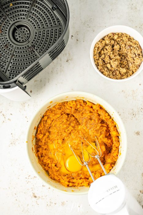 An air fryer with a bowl of mashed potatoes and a whisk.