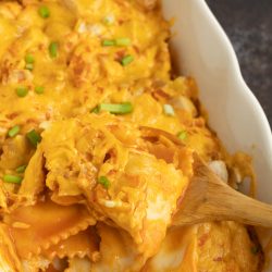 Cheesy chicken lasagna in a white dish with a wooden spoon.