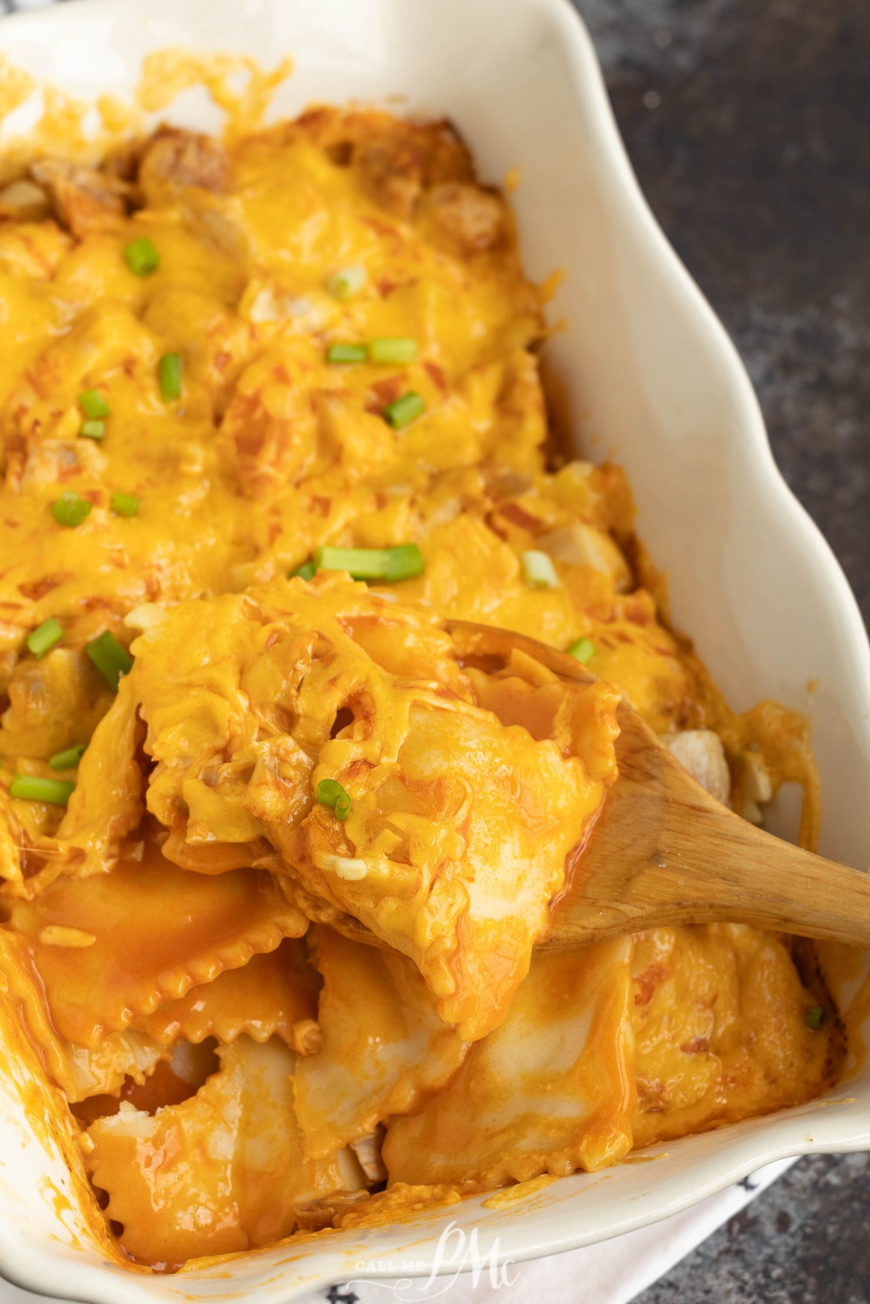 Cheesy chicken lasagna in a white dish with a wooden spoon.