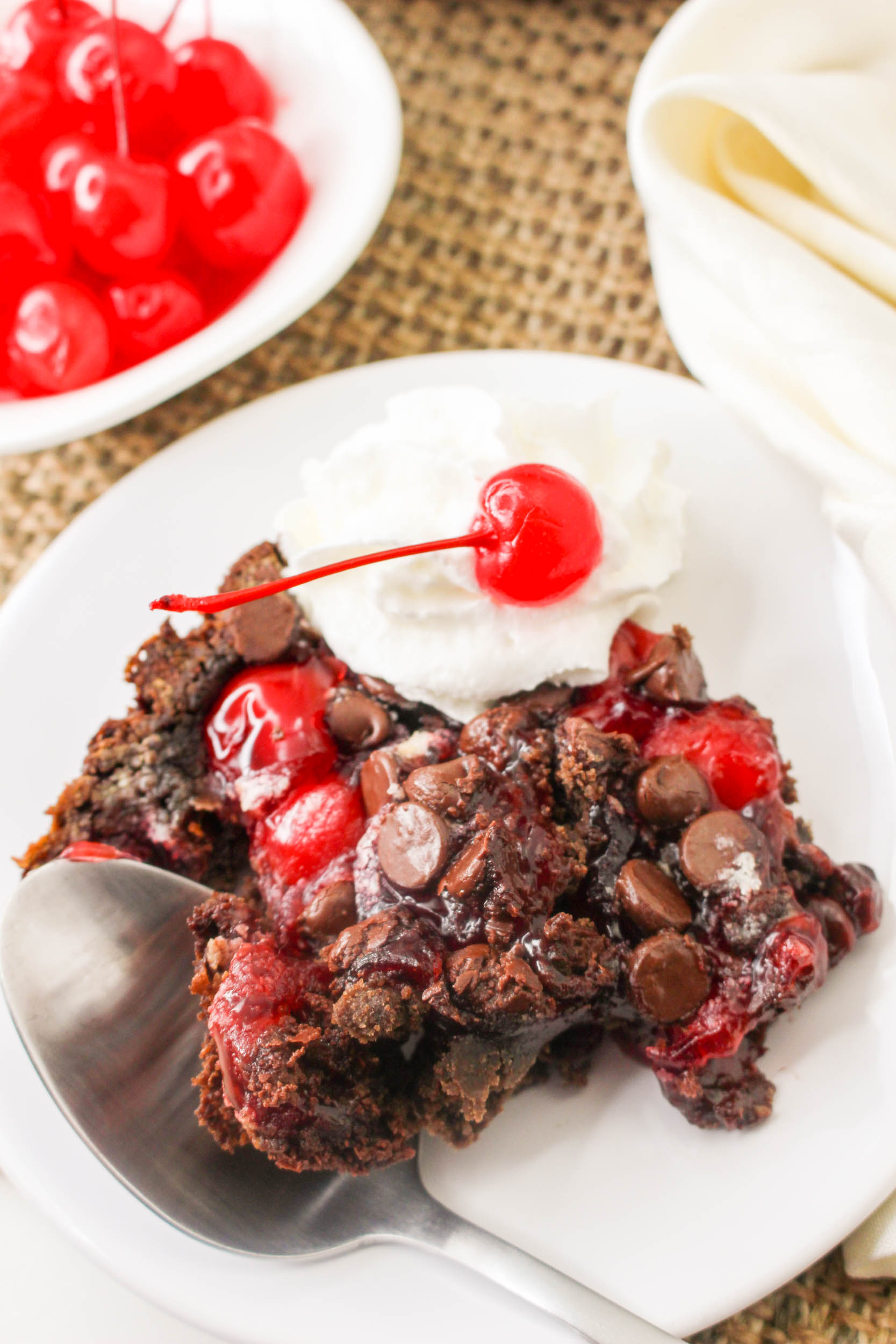 A piece of chocolate cherry pie with whipped cream and cherries on a plate.