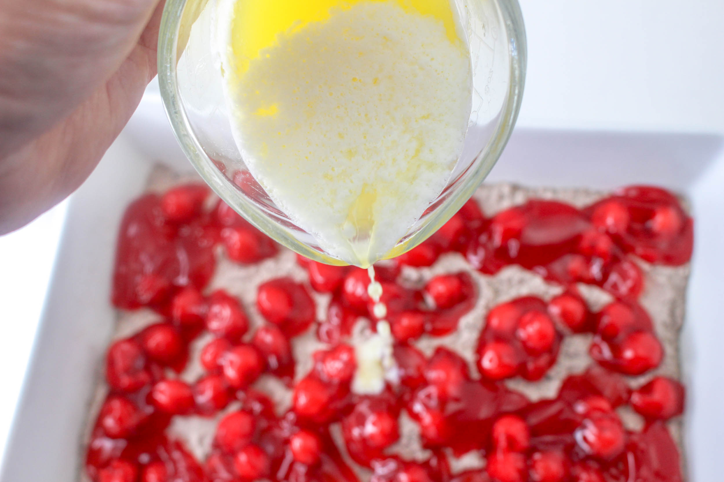 A person pouring an egg into a bowl of cherries.