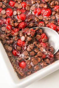 Chocolate cherry brownies in a white dish with a spoon.