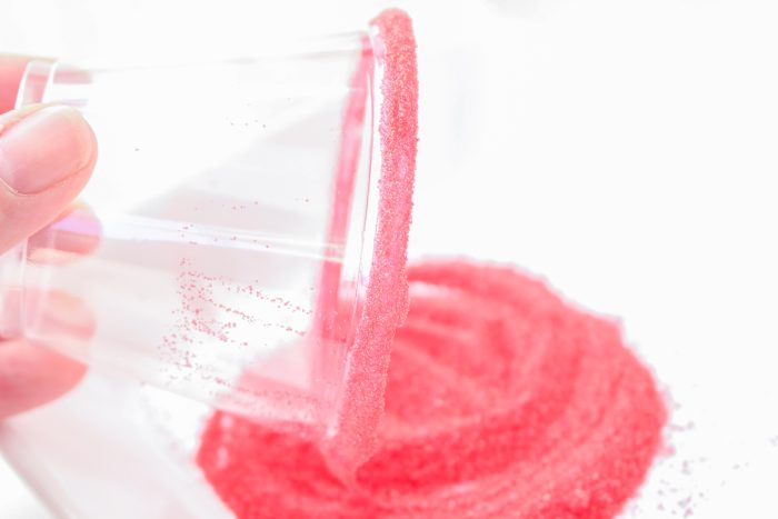 A person is pouring pink sand into a clear cup.