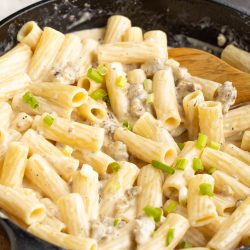 Penne pasta in a skillet with cheese and green onions.