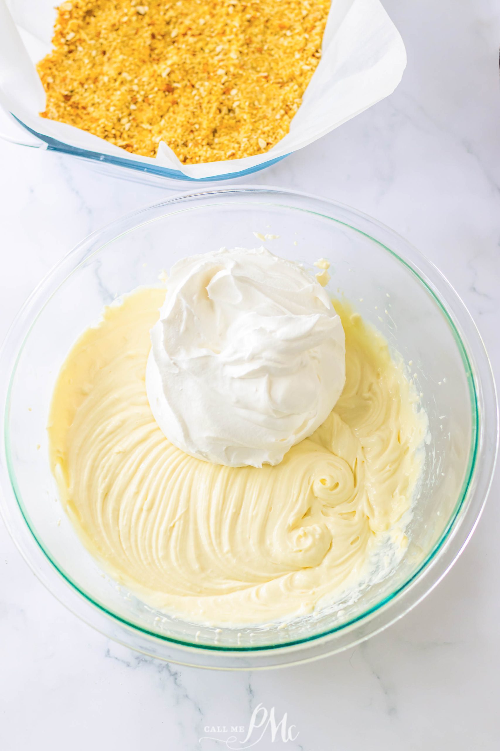 A bowl of whipped cream next to a bowl of graham cracker crumbs.