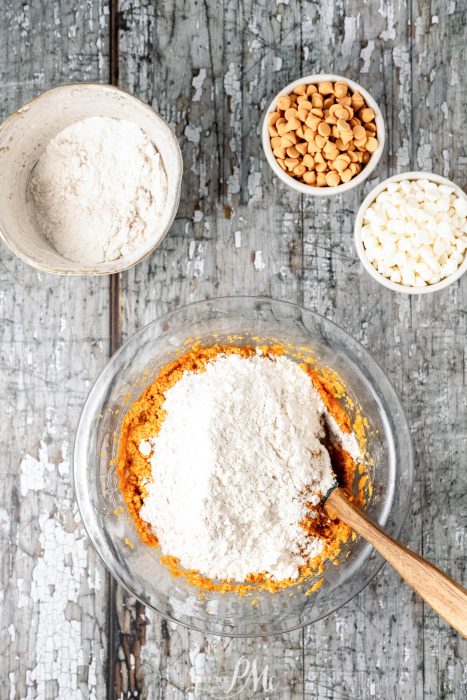 A bowl of flour, nuts and a wooden spoon on a wooden table.