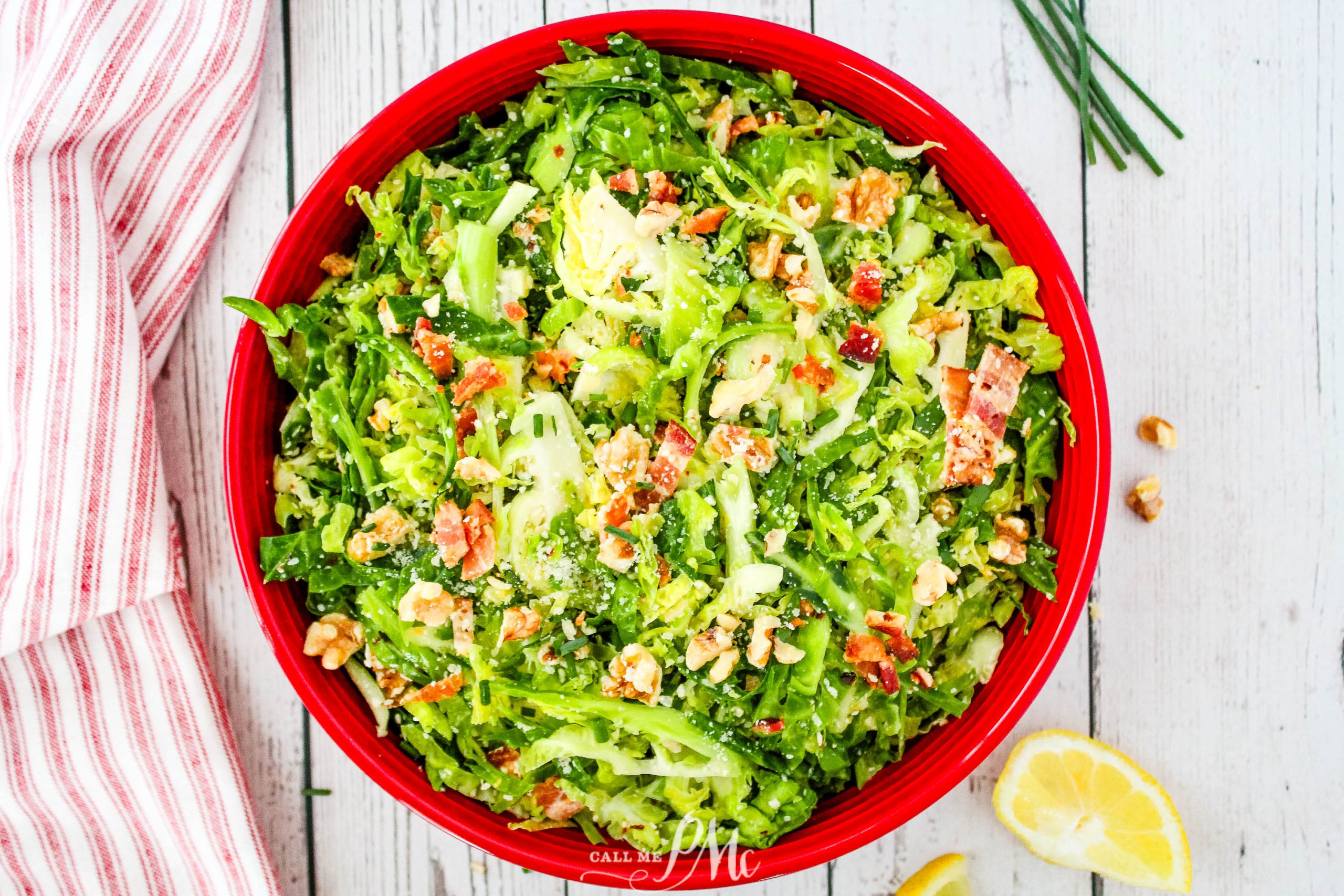 A red bowl with broccoli salad and lemon wedges.