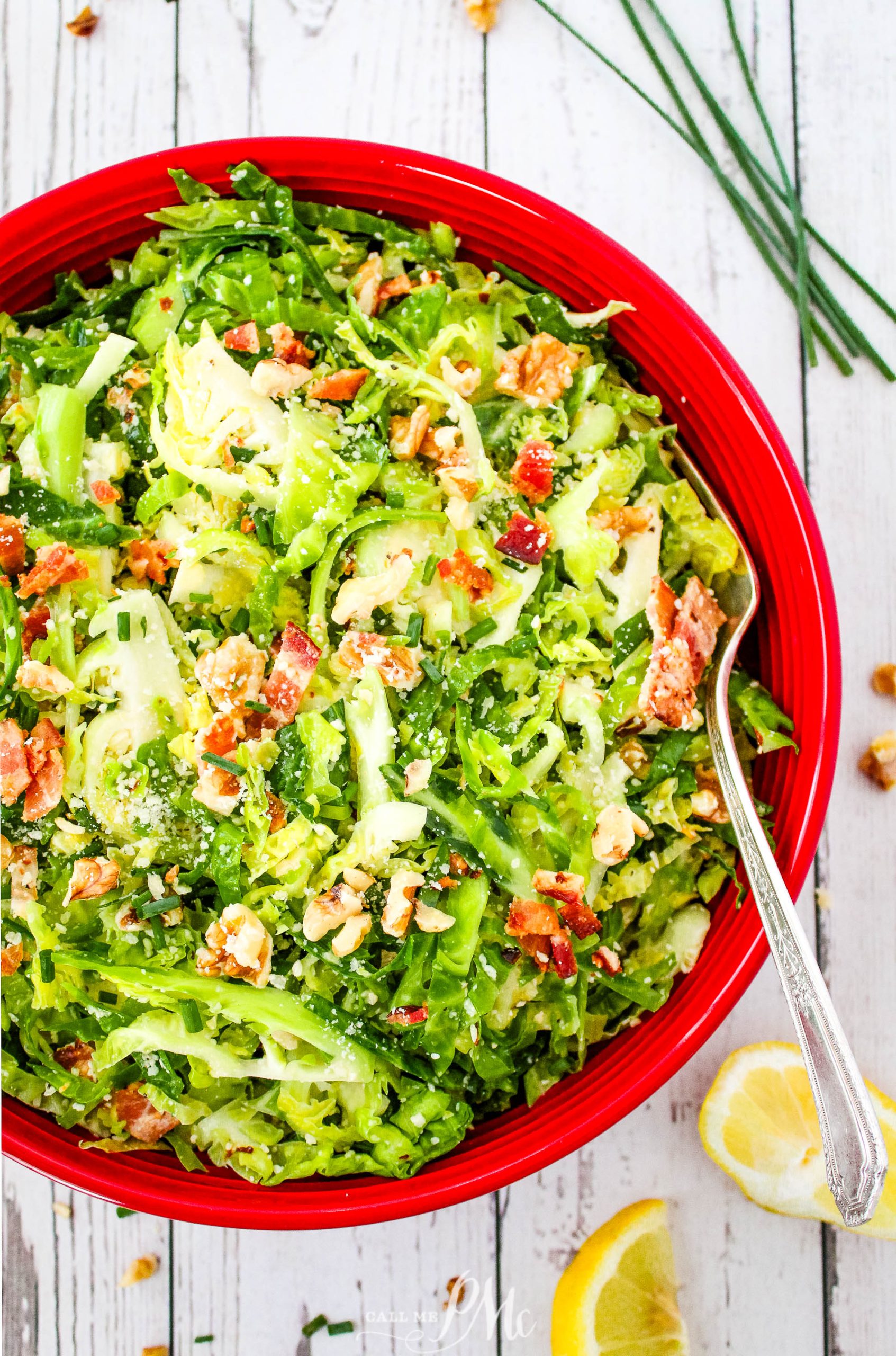 Brussels sprout salad in a red bowl with lemon wedges.