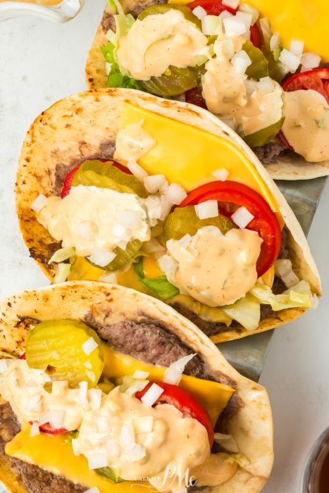 Three Viral Smash Burger Tacos with cheese, lettuce, tomatoes and pickles.