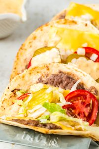 A plate of Viral Smash Burger Tacos with cheese, tomatoes and lettuce.