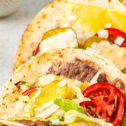 A plate of Viral Smash Burger Tacos with cheese, tomatoes and lettuce.