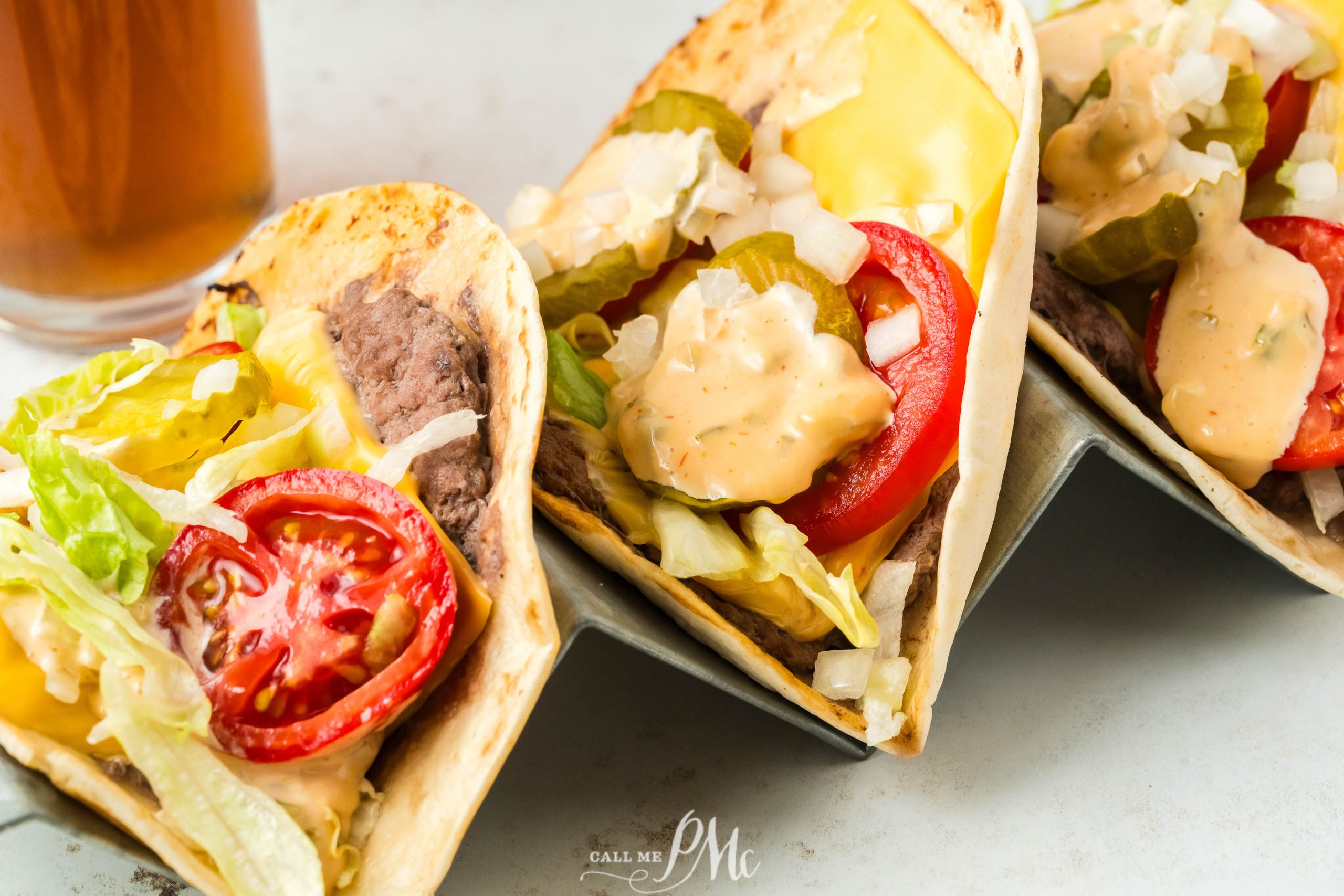 Three Viral Smash Burger Tacos are sitting on a table next to a beer.