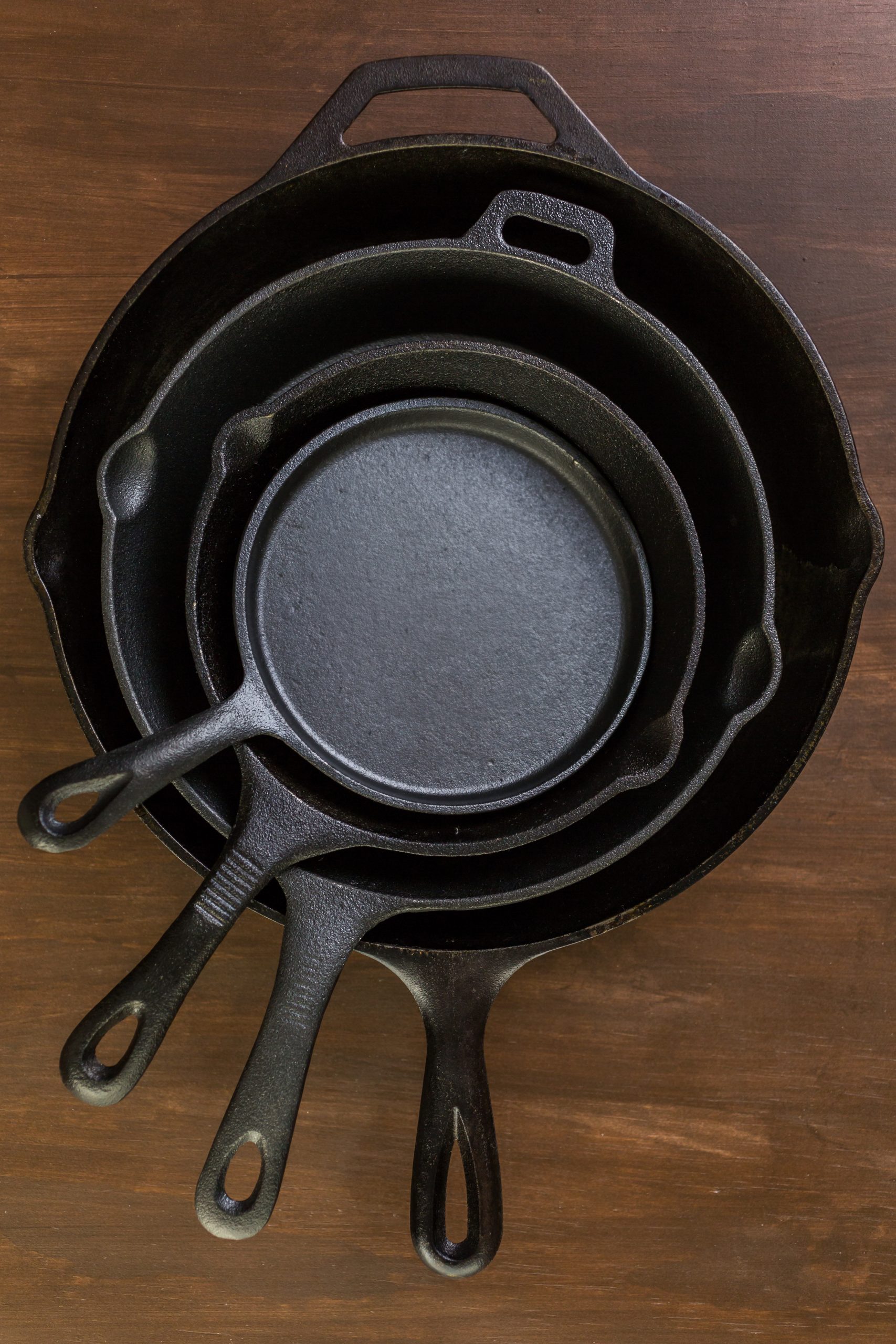 Three cast iron skillets on a wooden table.