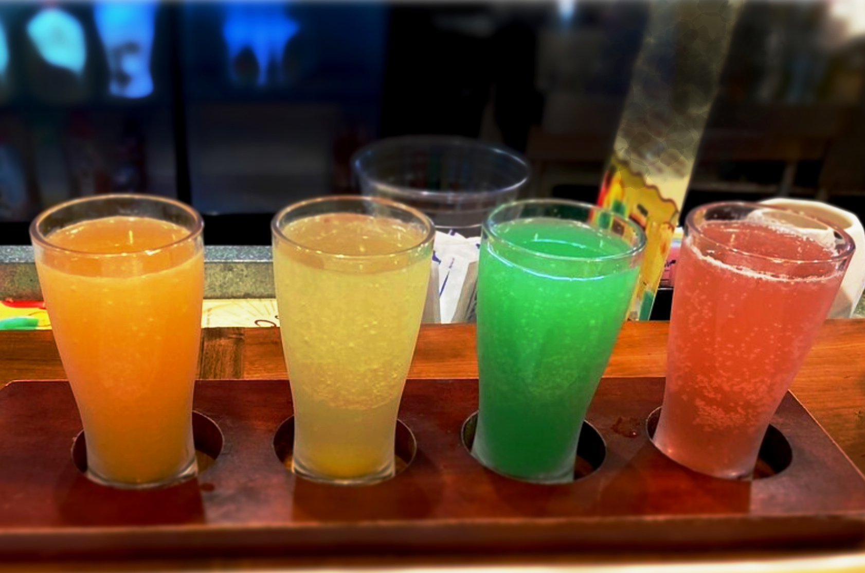 Four glasses of different colored drinks on a wooden tray.