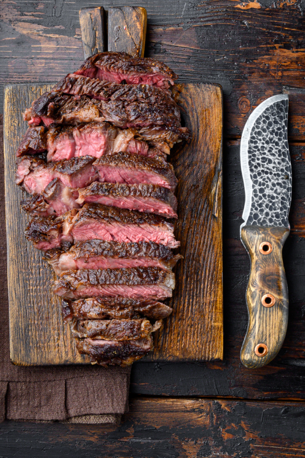 A cooked steak sliced on a cutting board with knife.
