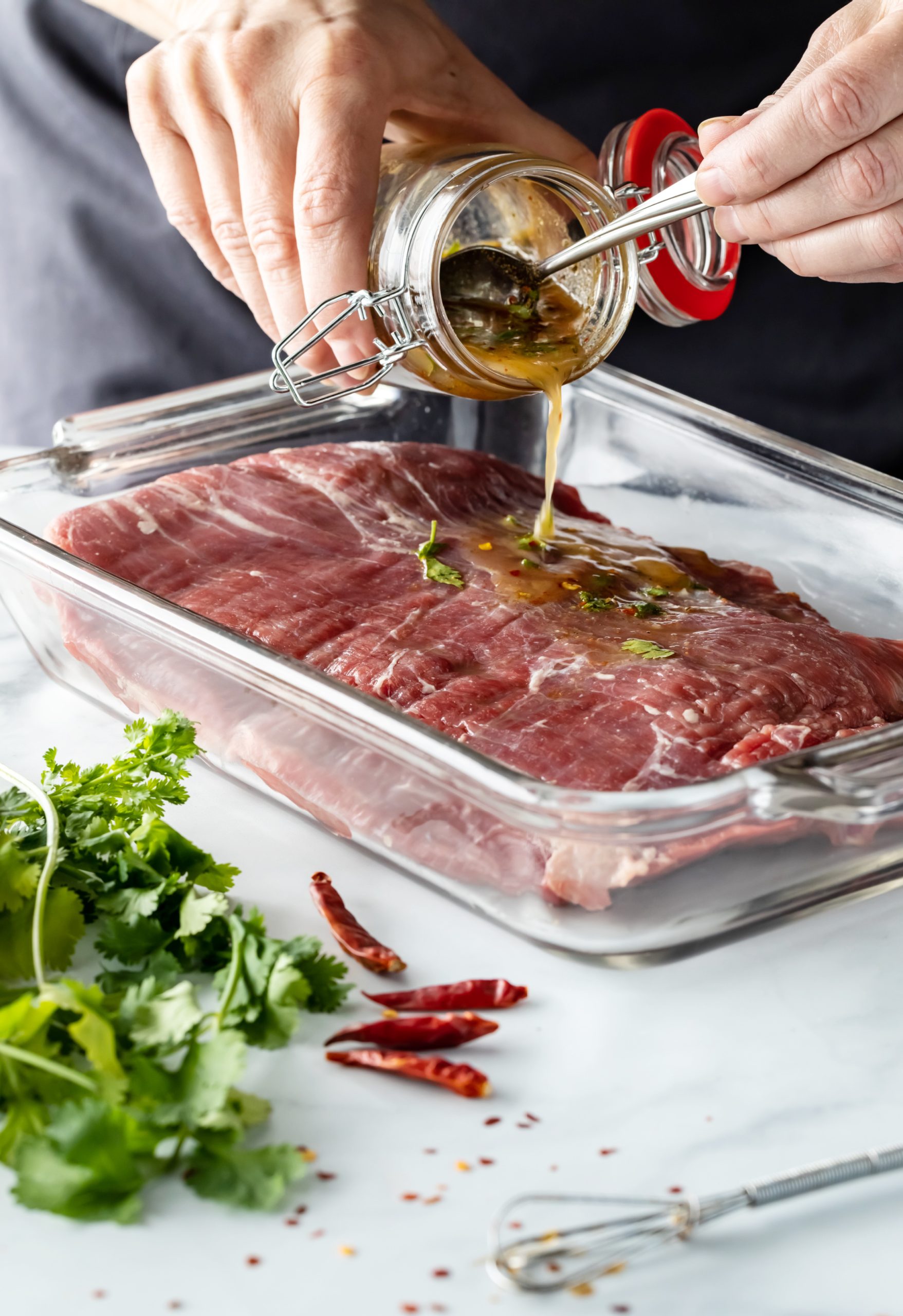 A person tenderizing and drizzling sauce on a piece of meat.