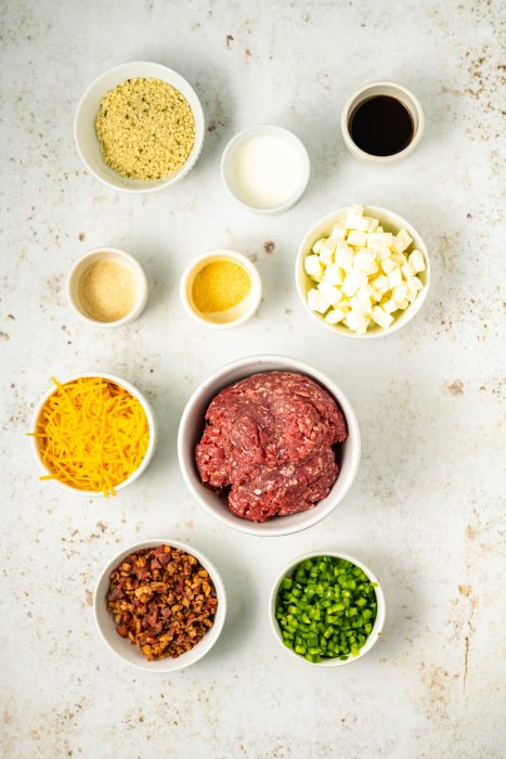 Ingredients for meatballs in bowls on a white surface.