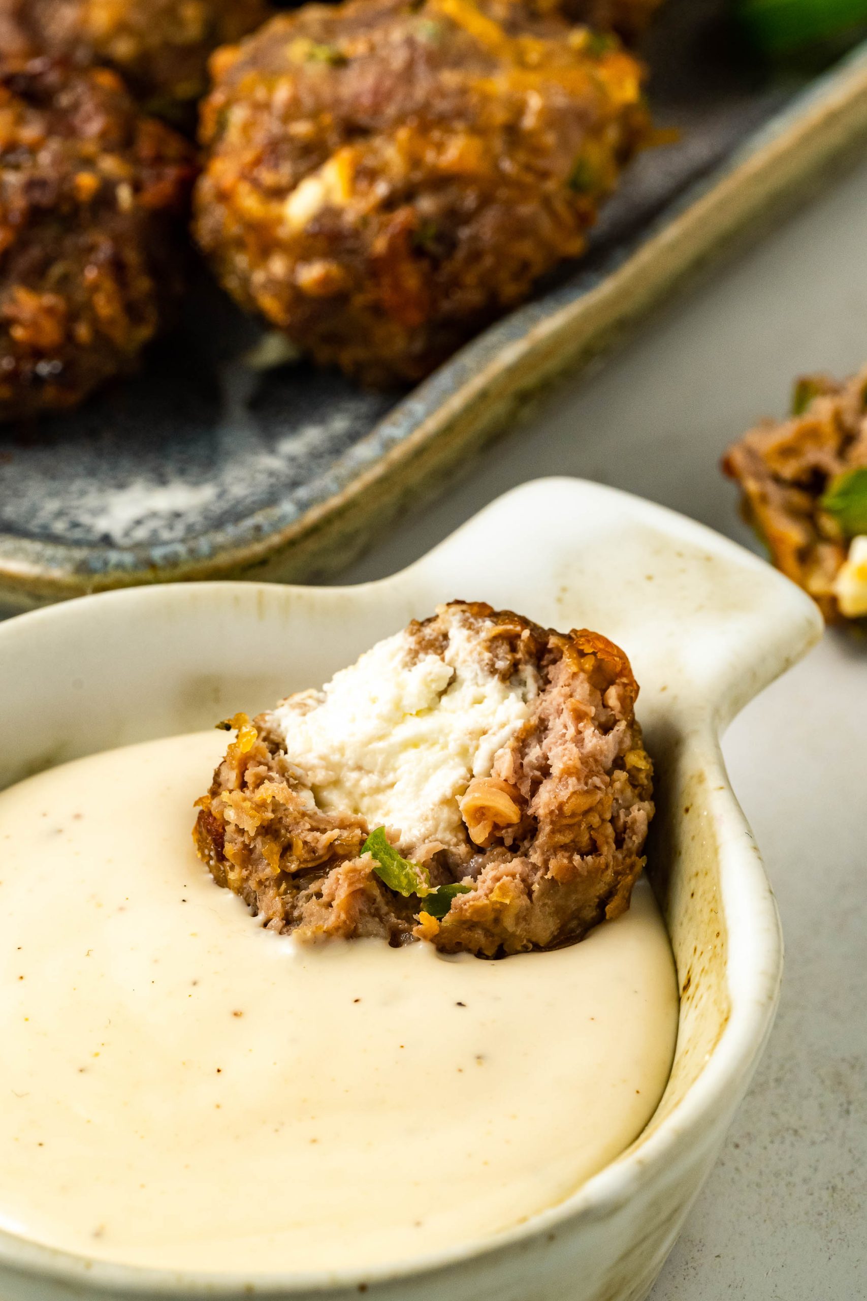 A bowl of Jalapeno Popper Meatballs with a sauce on the side.