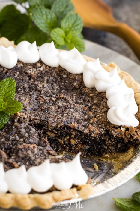A pie with whipped cream and mint leaves on a plate.