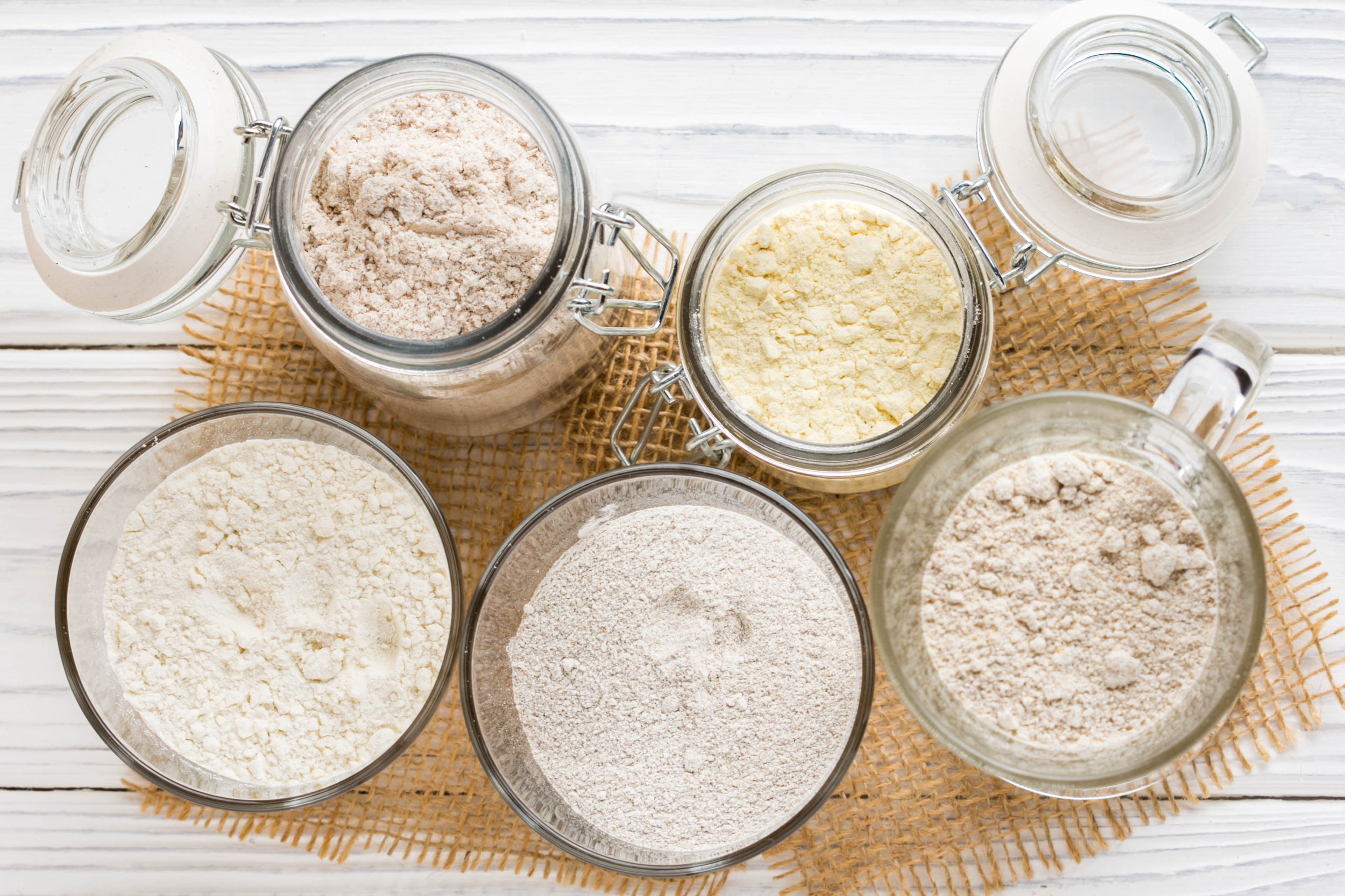 Various types of flour in glass jars on a wooden table.