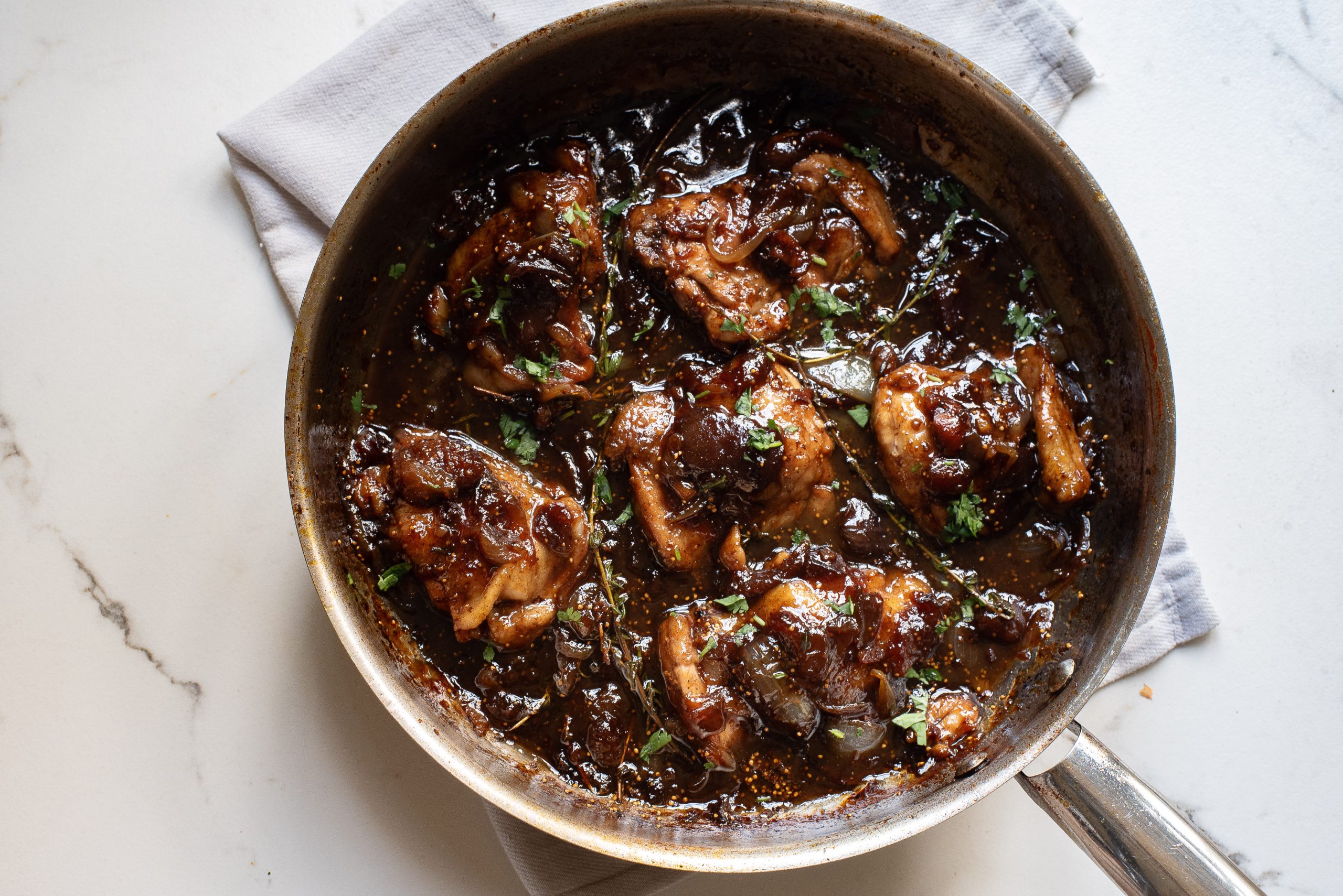 Chicken in a pan with sauce and herbs.