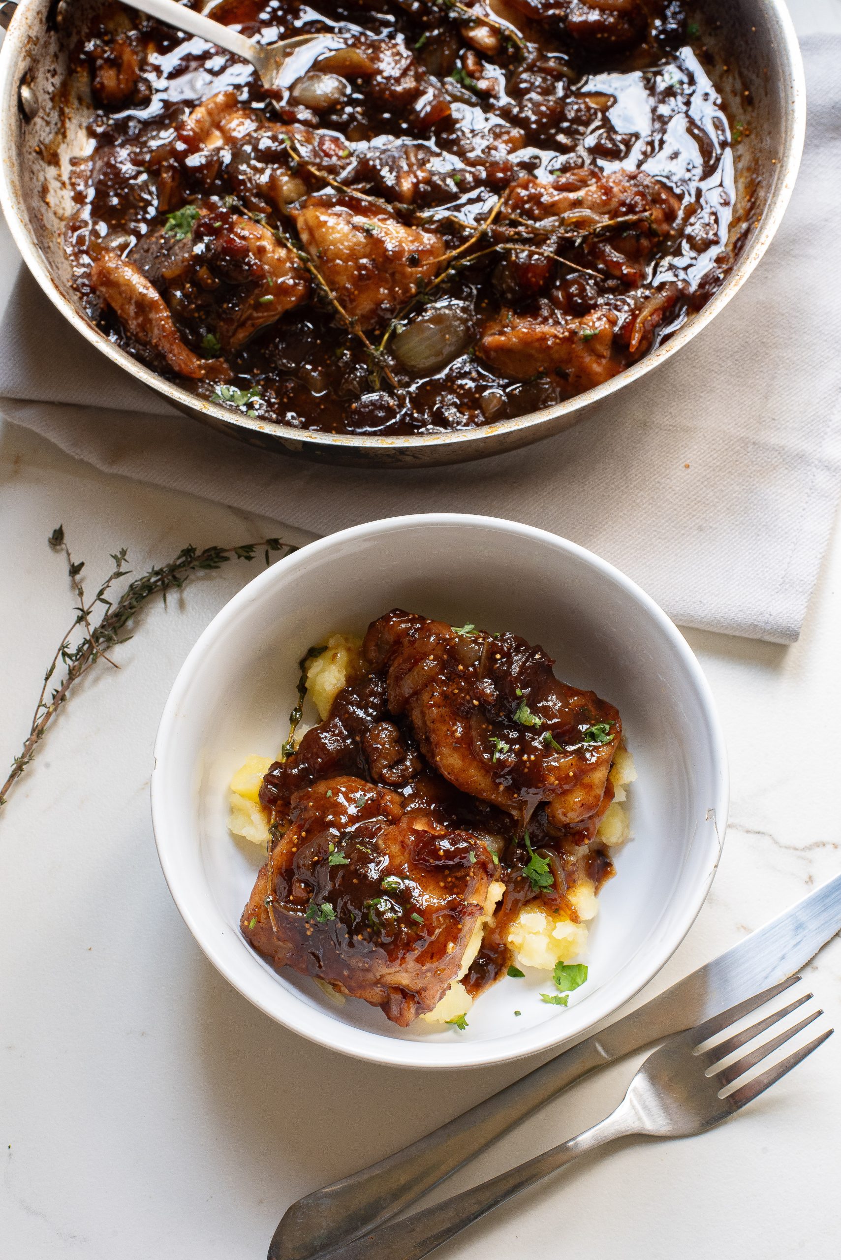 A bowl of chicken with gravy on a table next to a fork.