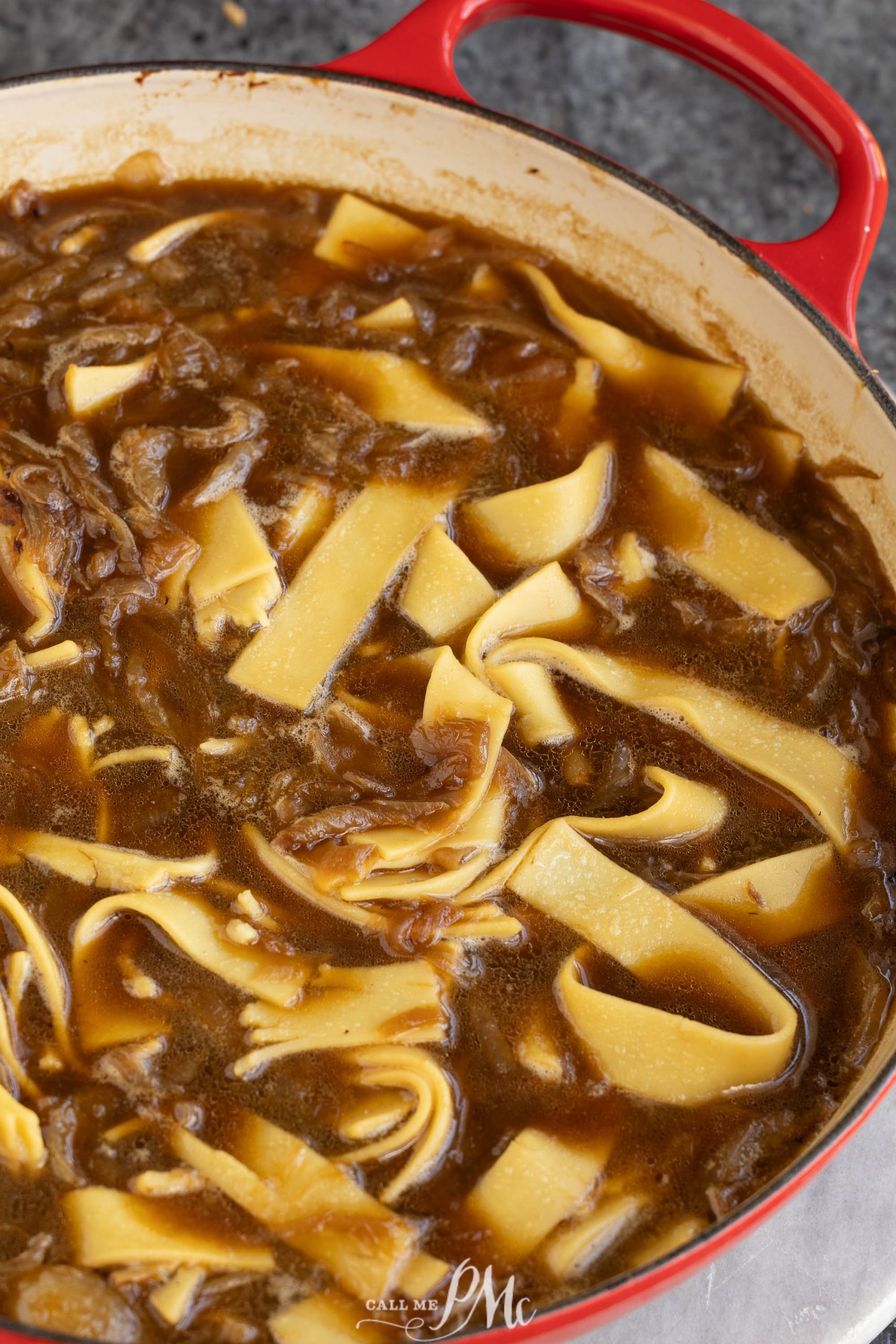 A pot full of beef and noodles in a red pot.