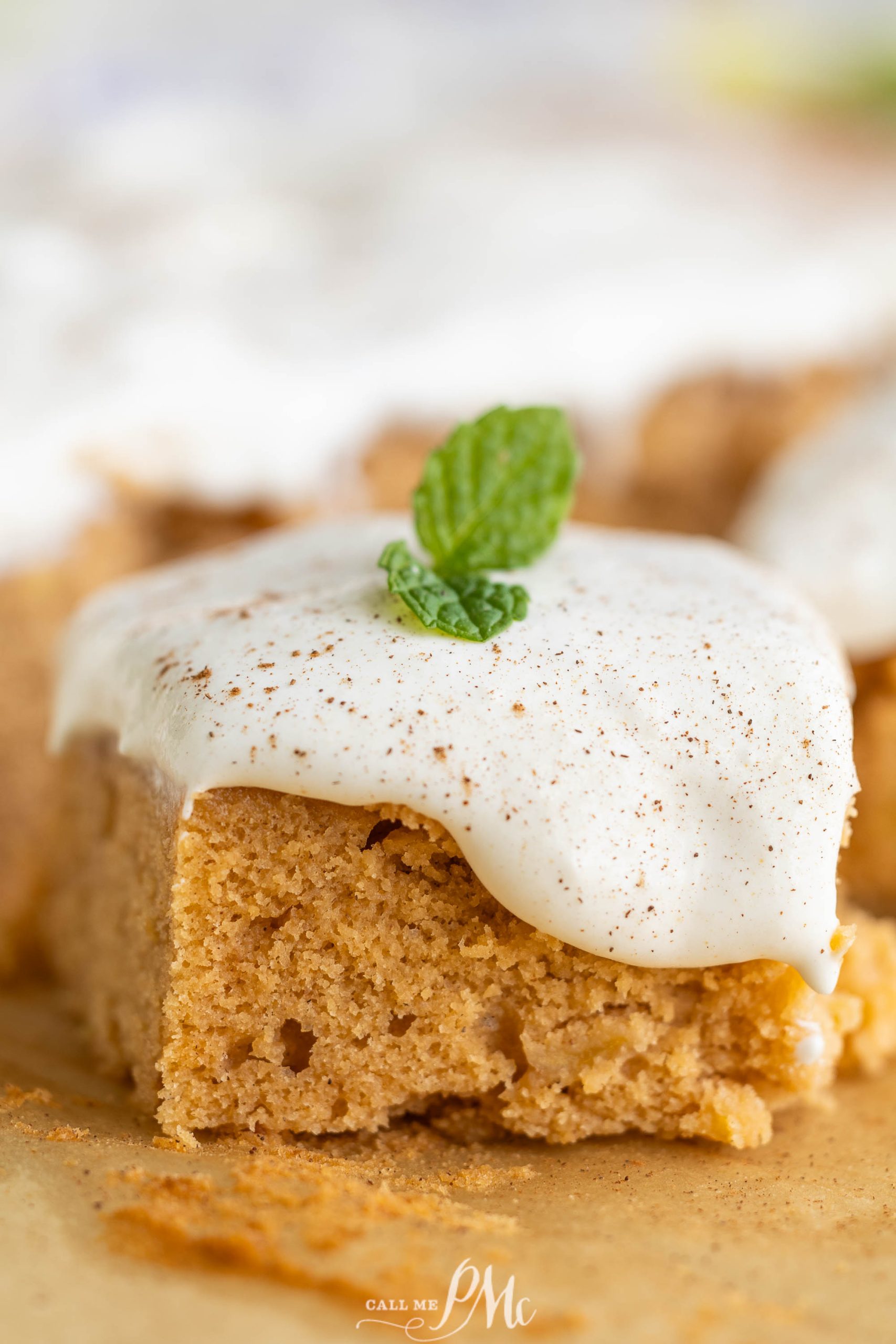 A slice of pumpkin cake with icing and mint leaves.