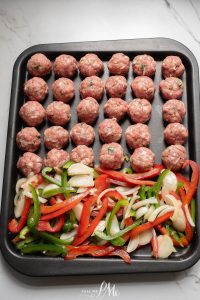 Meatballs on a baking sheet with peppers and onions.