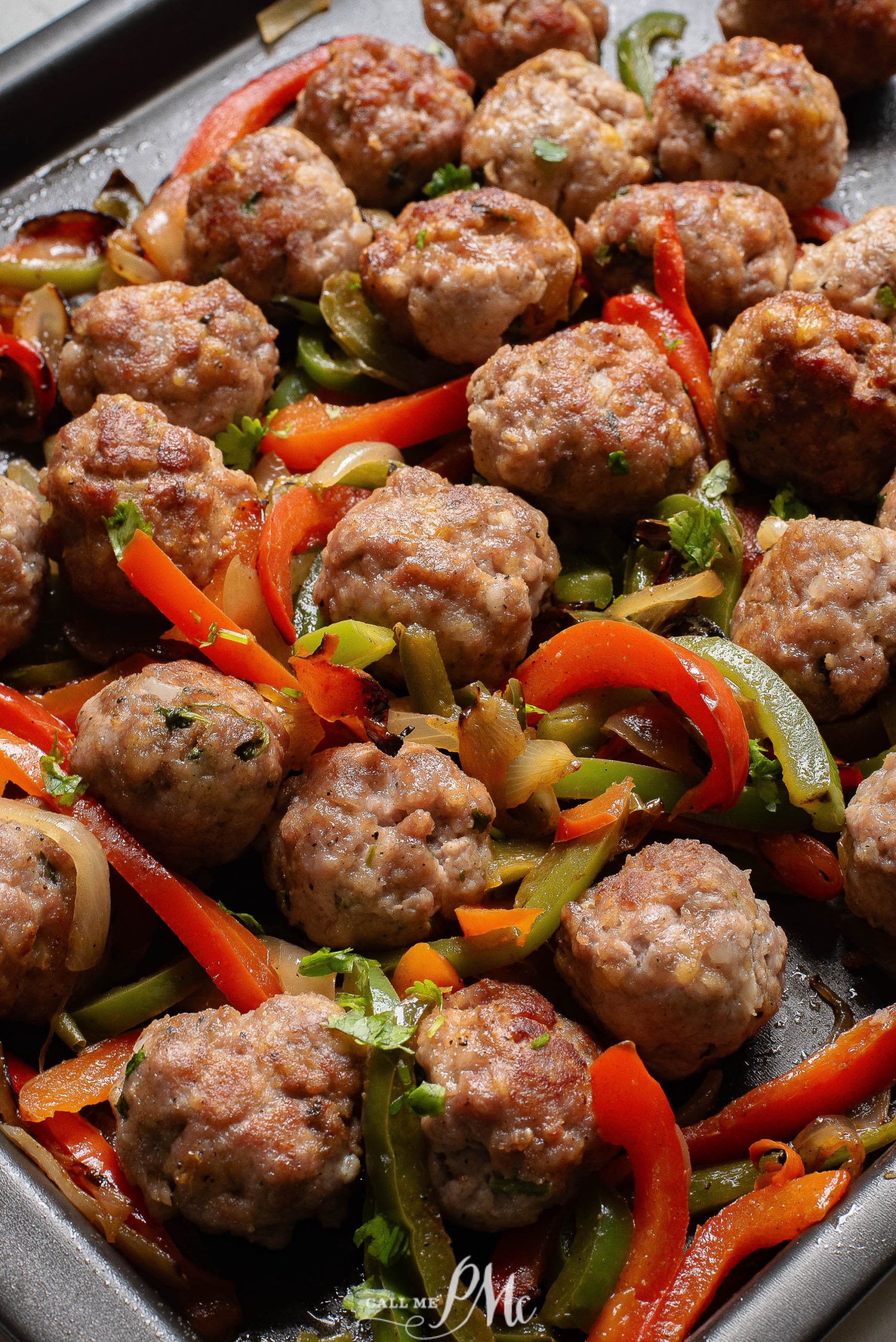 Meatballs with peppers and onions on a baking sheet.