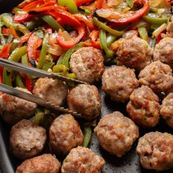 Meatballs with peppers and onions on a baking sheet.