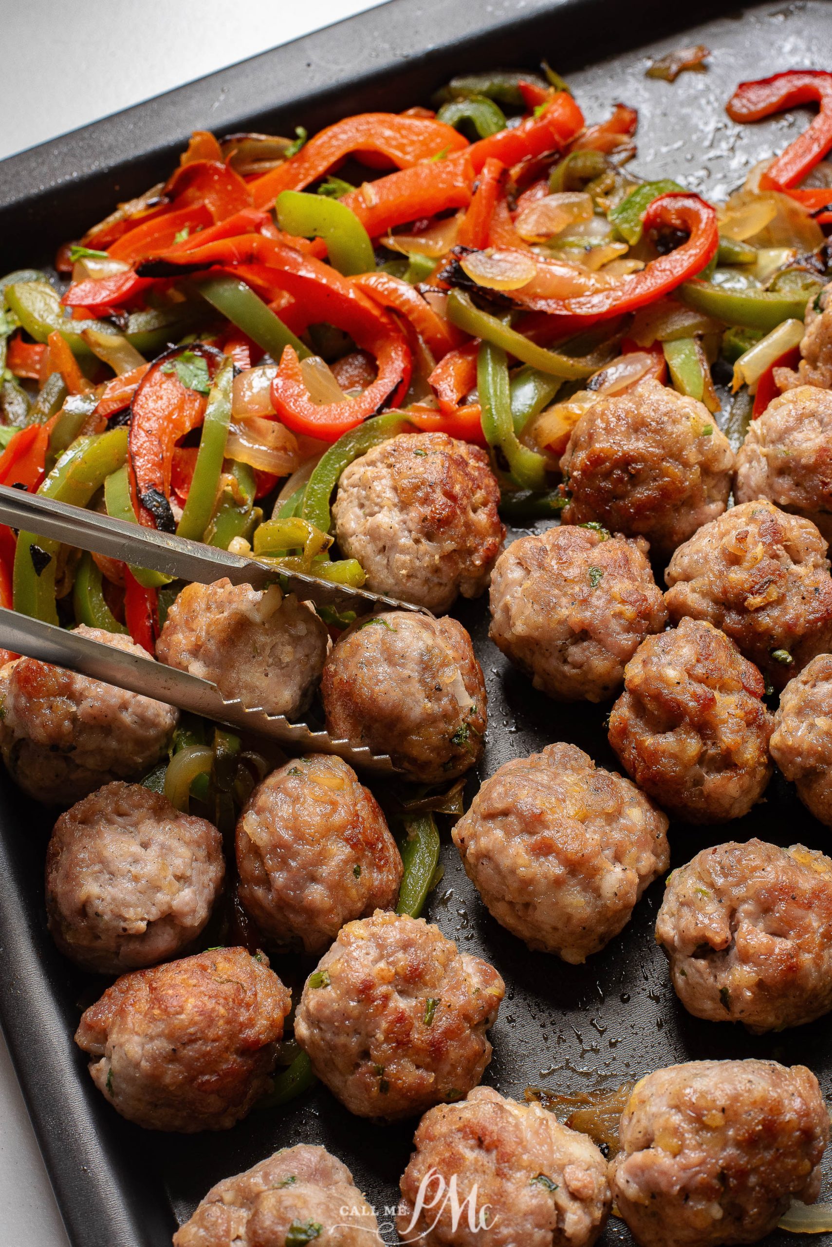 Meatballs with peppers and onions on a baking sheet.