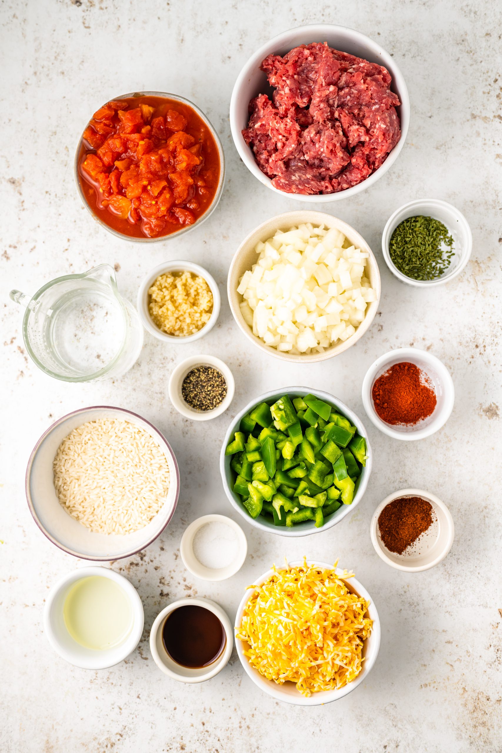 A bowl of ingredients for meatballs on a white background, including cheddar and beef.