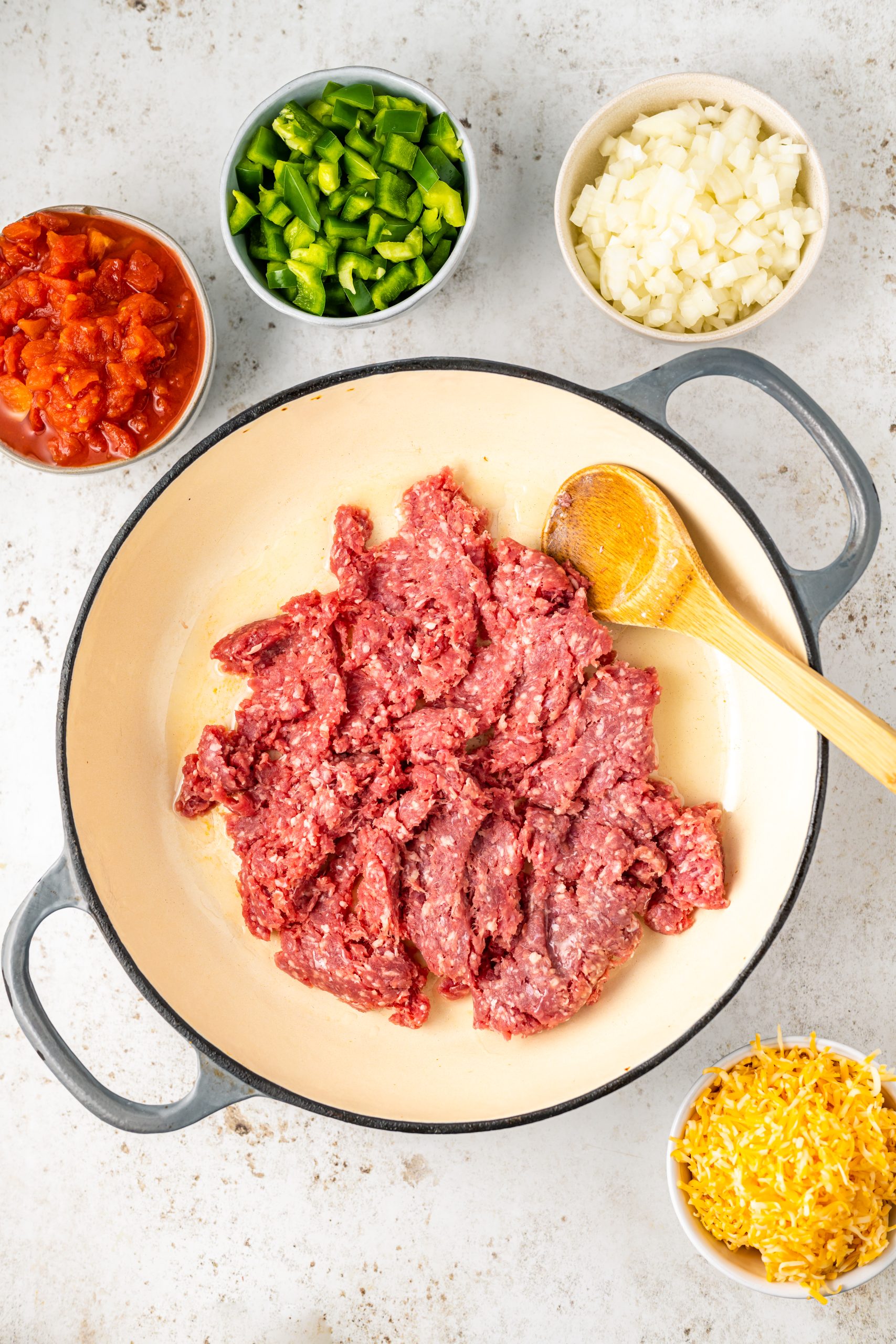 A skillet filled with ground beef, onions, peppers, Cheddar cheese  and other ingredients.