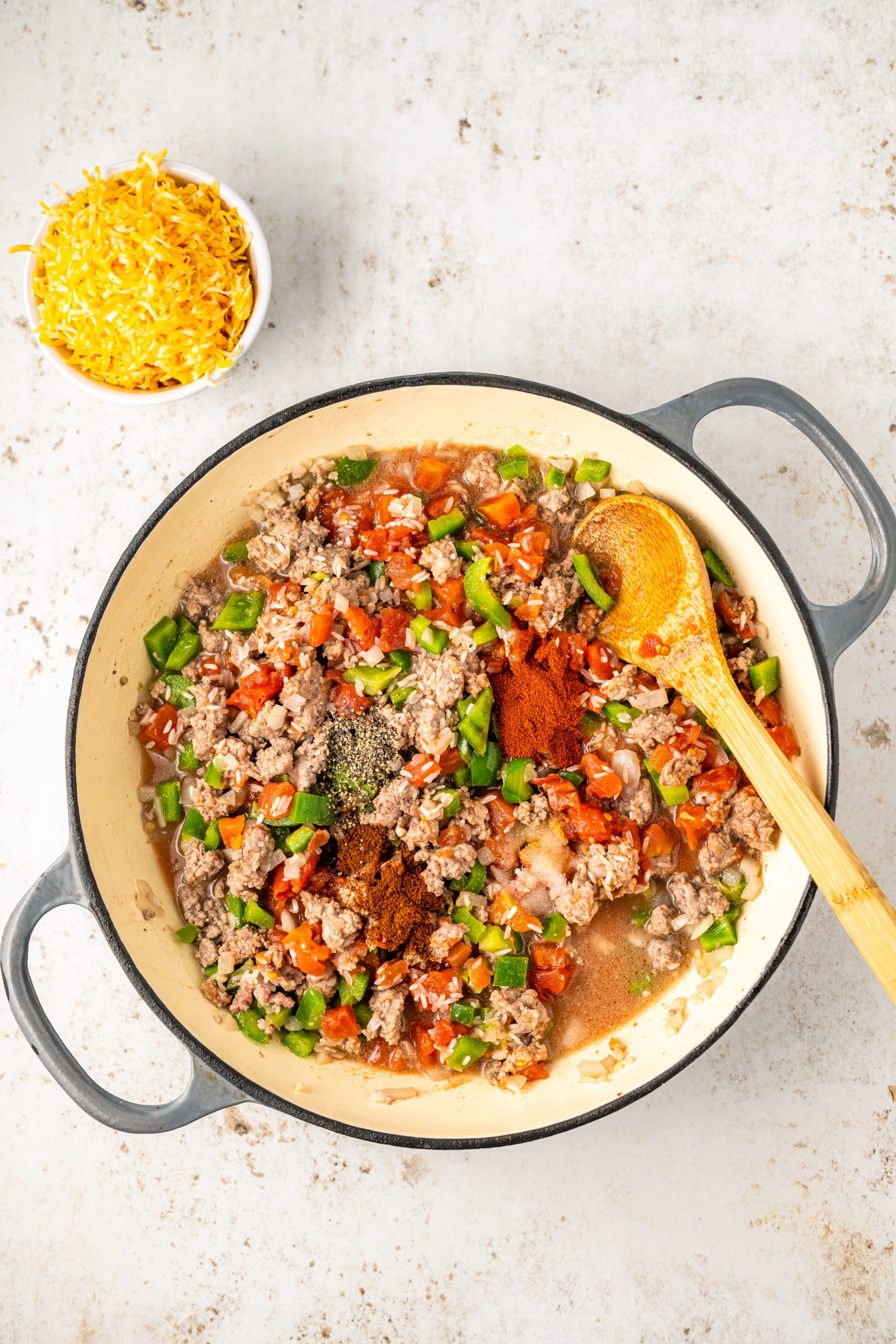 A pan full of hearty Cheddar Beef Texas Hash, cooked to perfection with a wooden spoon.