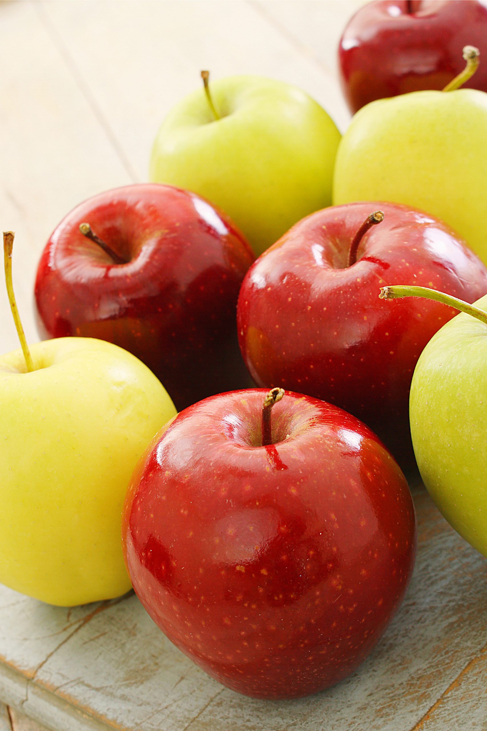 A group of red, yellow and green apples on a cutting board.