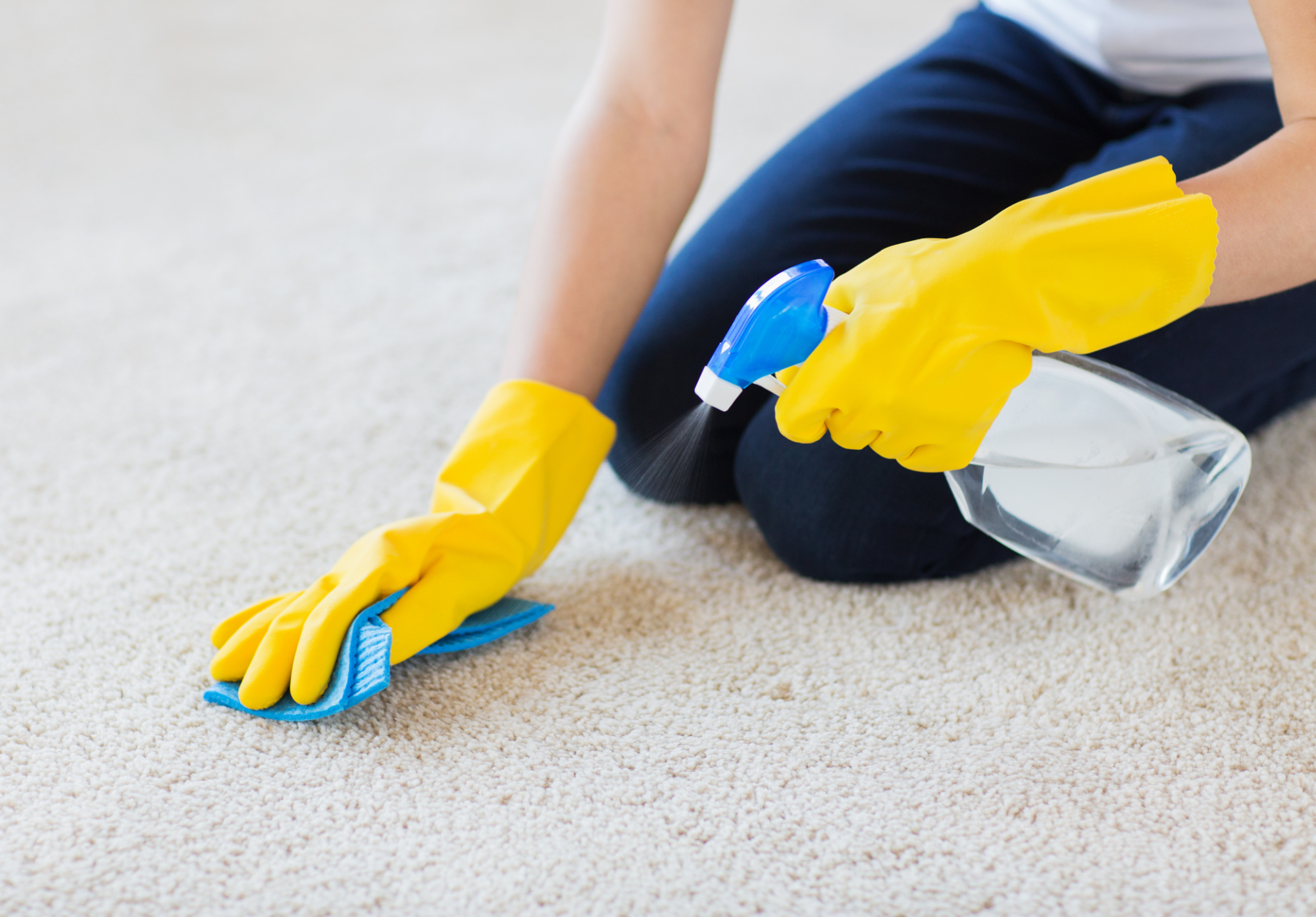 A woman wearing yellow gloves cleaning the carpet.