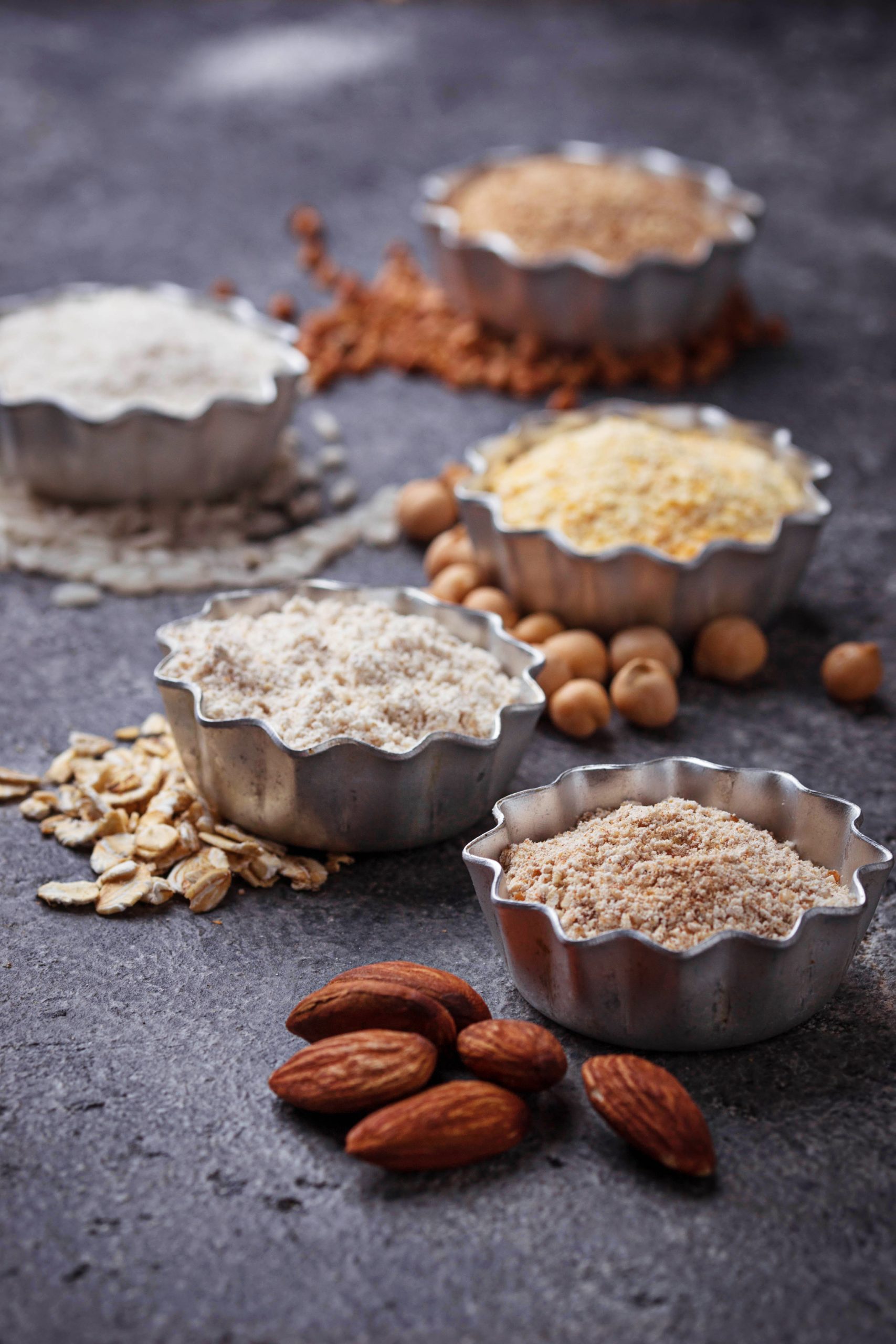 Several bowls of oatmeal, almonds, and oats on a dark background.