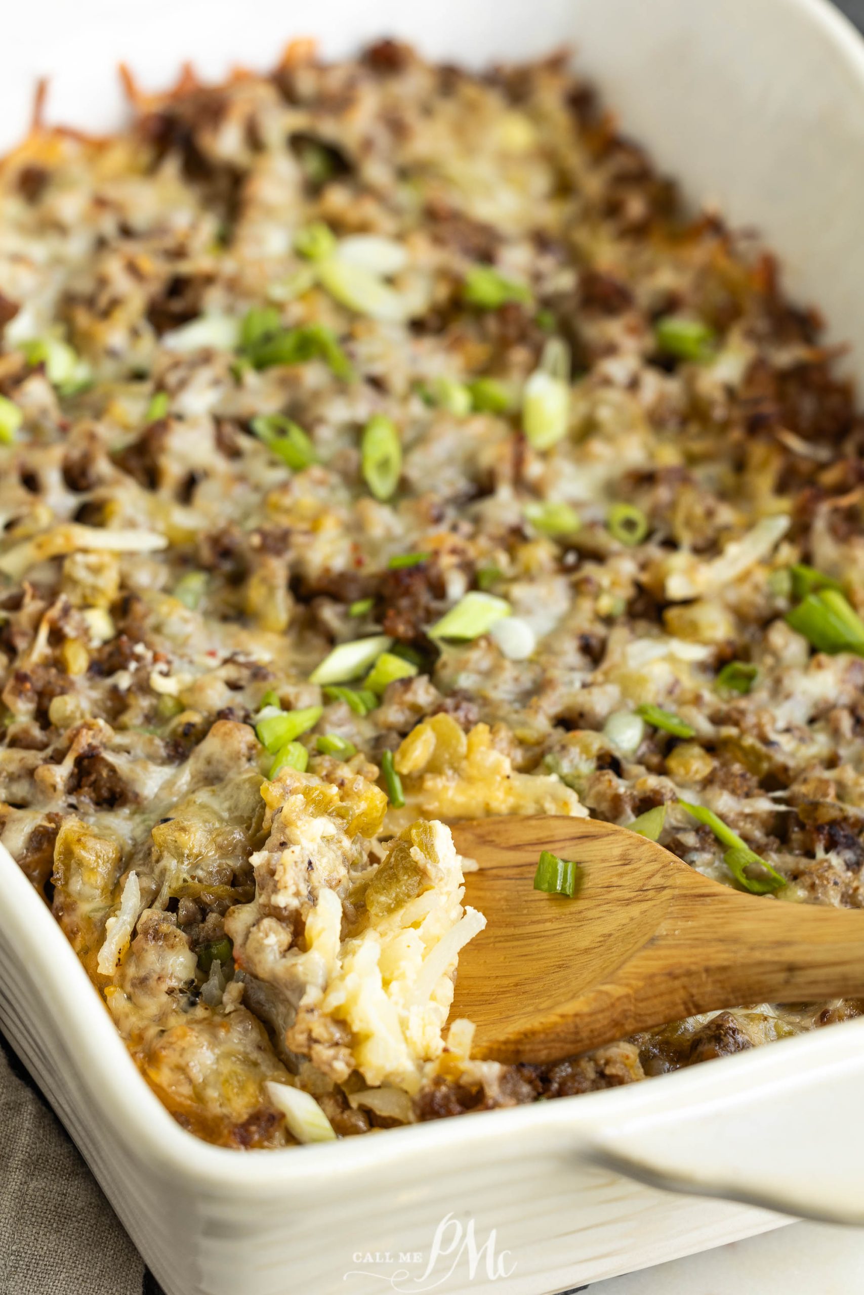 A Overnight Sausage Hash Brown Casserole with a wooden spoon in it.