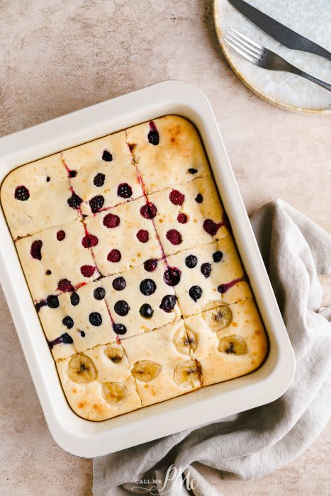 A baking dish with sheet pan pancakes with berries and bananas on it.