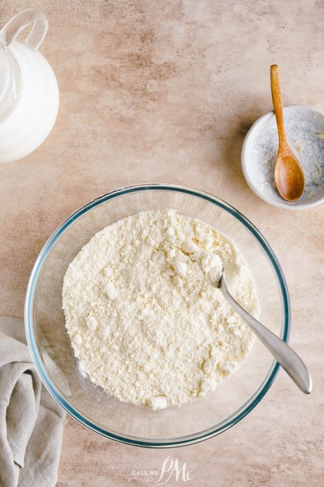 A glass bowl filled with flour and a wooden spoon.