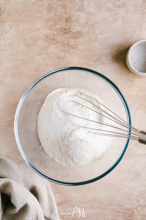 A bowl filled with flour and a whisk.